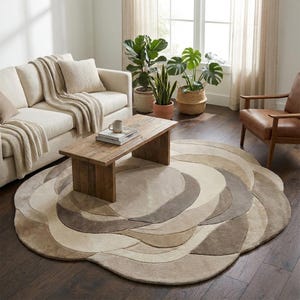 May include: A circular rug with a layered, floral design in neutral tones. The rug's colour palette includes beige, tan, and grey. It is placed in a living room with a wooden coffee table and a cream-coloured sofa. The rug's diameter is approximately 200 cm.