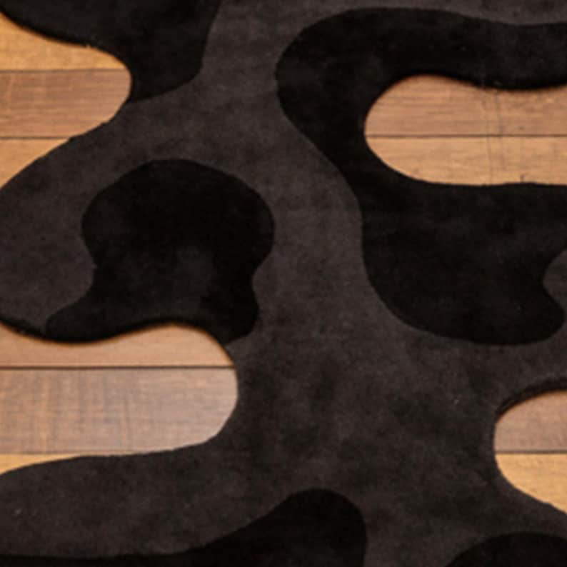 Irregular Black Hand-Tufted Wool Runner Rug with Abstract Wavy Shape, placed on a wooden floor in a modern entryway with stairs.