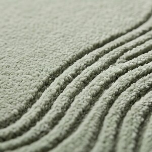 May include: A sage green rug featuring a thick, high-pile texture with deep, carved parallel wave patterns. The soft, plush material creates a dimensional surface with alternating ridges and valleys that emphasize the curved, flowing design.