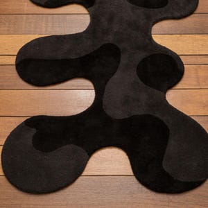 Irregular Black Hand-Tufted Wool Runner Rug with Abstract Wavy Shape, placed on a wooden floor in a modern entryway with stairs.