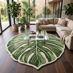 May include: A large, circular area rug shaped like a monstera leaf, featuring deep green and light green textured segments with cut-out details and a cream-colored border, placed on a dark wood floor beneath a glass-topped coffee table.