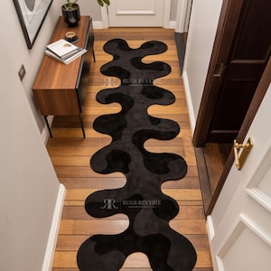 Irregular Black Hand-Tufted Wool Runner Rug with Abstract Wavy Shape, placed on a wooden floor in a modern entryway with stairs.