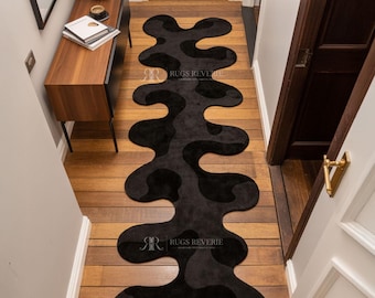 May include: A black, abstract-shaped runner rug with a unique, flowing design. The rug is placed on a wooden floor in a hallway. The text "RUGS REVERIE" is visible on the rug.