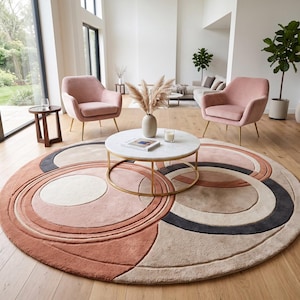 Könnte beinhalten: Ein großer runder Teppich mit einem geometrischen Muster aus überlappenden Kreisen und Bögen in den Farben Terrakotta, Beige, Creme und Anthrazit. Der Teppich hat eine strukturierte, getuftete Oberfläche und liegt auf einem hellen Holzboden.