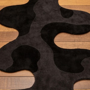 Irregular Black Hand-Tufted Wool Runner Rug with Abstract Wavy Shape, placed on a wooden floor in a modern entryway with stairs.