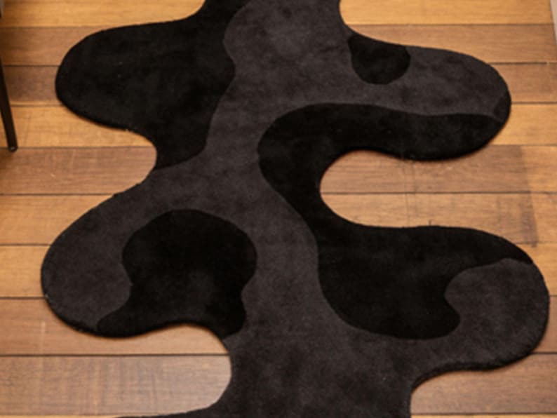 Irregular Black Hand-Tufted Wool Runner Rug with Abstract Wavy Shape, placed on a wooden floor in a modern entryway with stairs.
