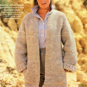 Könnte beinhalten: Eine hellbeige, grob gestrickte Jacke mit vertikalen Taschen. Die Jacke hat lange Ärmel und einen Kragen. Der Text auf dem Bild lautet "Easy but stylish length garter stitch jacket with vertical pockets."