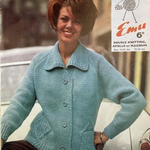 May include: A light blue knitted cardigan with a collar and three buttons. The cardigan has two front pockets and is worn by a person. The image also includes text that reads "Emu" and "Double Knitting, Apollo or Magnum".