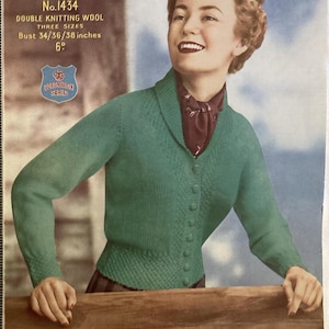 May include: Vintage knitting pattern cover showing a woman in a green cardigan. The cover reads "Sirdar No.1434 DOUBLE KNITTING WOOL" and bust sizes 86/91/97 cm. The woman smiles, with a light blue background. A vintage fashion item.