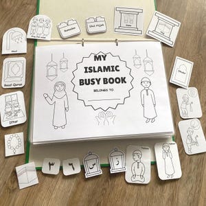 Op de afbeelding: Een open "My Islamic Busy Book" met een groene band en diverse activiteitkaarten. Het boek bevat illustraties van islamitische praktijken en symbolen, waaronder een moskee, gebed en de Koran. Extra kaarten tonen cijfers en Arabische letters.