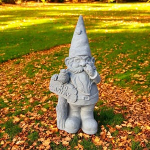 May include: A gray garden gnome statue with a pointed hat, beard, and boots. The gnome holds a sign that reads "GO AWAY" and has an owl perched on a wooden post. The statue is set in a garden with fallen leaves.