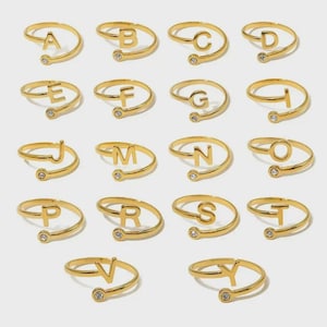 Peut inclure: Anneaux réglables dorés, chacun orné d'une lettre de l'alphabet. Les bagues présentent un design en spirale et un petit accent de pierre précieuse transparente. Les lettres A, B, C, D, E, F, G, H, J, M, N, O, P, R, S, T, V et Y sont affichées.