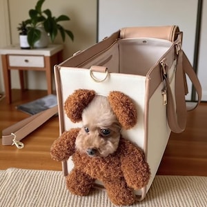 May include: A cream and tan dog carrier with a rectangular shape. The carrier features a handle and a shoulder strap. A small brown dog is visible, peeking out of the carrier with its head and front paws showing.
