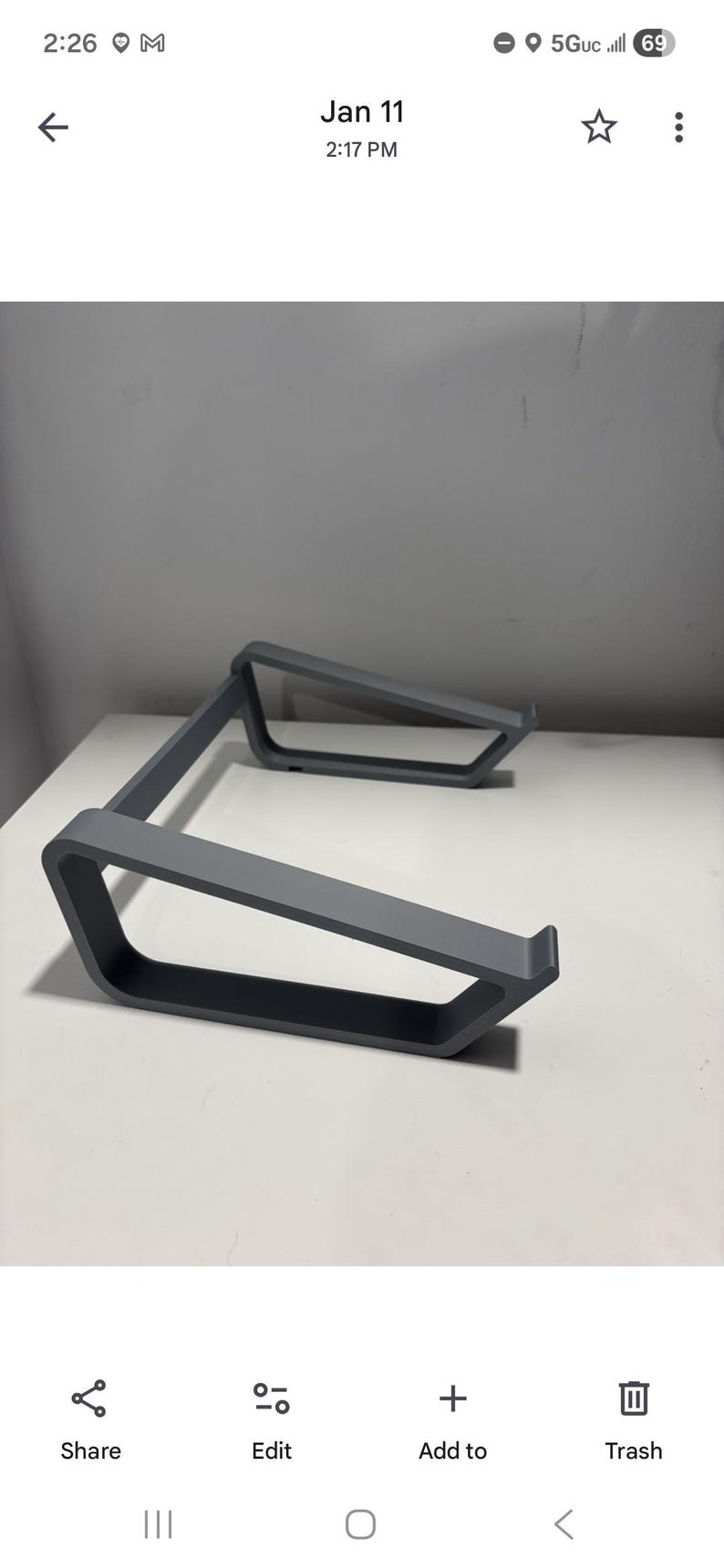 May include: A gray laptop stand with a minimalist design. The stand is made of a solid material and features a rectangular base with angled supports. It is designed to elevate a laptop for improved ergonomics.