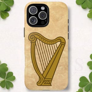 May include: A smartphone case with a light tan, textured background featuring a centered, dark gold illustration of a harp. The case has a black camera module cutout at the top left, containing three circular lenses and a flash component.