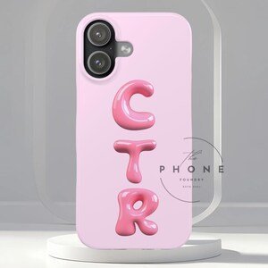 Puede incluir: Funda de teléfono rosa claro con las letras "CTR" en fuente de burbujas 3D. La funda tiene una cámara de doble lente y un botón plateado. El logotipo de The Phone Foundry es visible en el lado derecho.