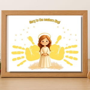 May include: A framed print with a cartoon angel in a white dress and a halo, with yellow handprints on either side. The text "Glory to the newborn King!" is above the angel. The print is in a wooden frame.