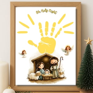 May include: A framed print with a Christmas theme. The artwork features a yellow handprint with radiating lines, angels, and a nativity scene. The text "Oh Holy Night" is at the top. A small Christmas tree and candle are in the foreground.