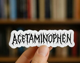 May include: A white sticker featuring the word "ACETAMINOPHEN" in a black, gothic font. The sticker is held up by a hand, with a blurred bookshelf in the background.