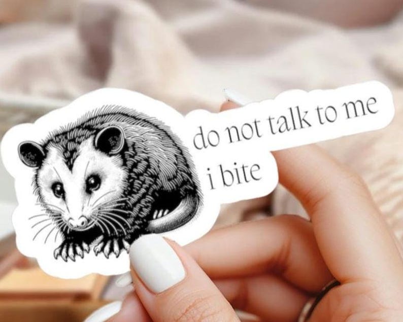 May include: A black and white sticker featuring an opossum illustration. The opossum is surrounded by the text "do not talk to me i bite". The sticker has a white background.