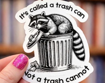 Könnte beinhalten: Ein gestanzter Aufkleber mit einer schwarz-weißen Illustration eines Waschbären, der auf einer Mülltonne aus Metall mit leicht geöffnetem Deckel sitzt. Der Text oben lautet It's called a trash can und unten Not a trash cannot.