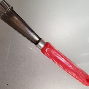 May include: A red handled stainless steel melon baller with a fluted edge.