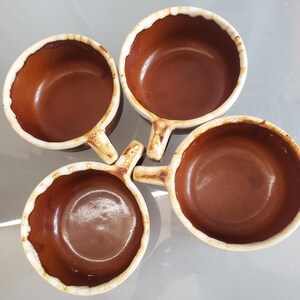 May include: Four brown ceramic bowls with handles. The bowls have a round shape with a slightly scalloped rim and a handle on one side. The interior of the bowls is a darker brown, while the rim and handle are a lighter, off-white color.
