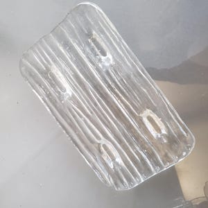 May include: A clear glass dish with a textured surface that resembles wood grain. The dish has three indentations on the surface.