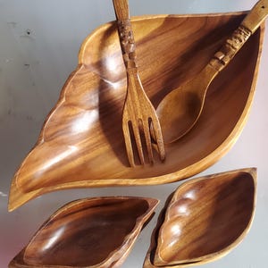 May include: A set of four wooden bowls, including a large leaf-shaped bowl and two smaller bowls. The set also includes a wooden fork and spoon.
