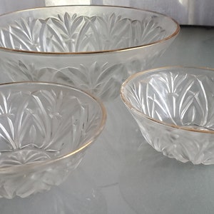 May include: Set of three clear glass bowls with a gold rim and a frosted, etched design. The bowls are nested inside each other, with the largest bowl on the bottom and the smallest bowl on top.
