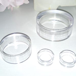 May include: A collection of clear acrylic ring-shaped objects of varying sizes. The objects are transparent, allowing light to pass through. The arrangement includes two larger rings and three smaller rings, suitable for display or decorative purposes.