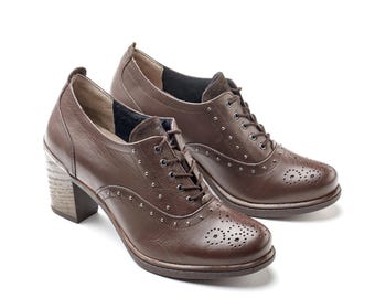 May include: A pair of brown leather heeled oxfords. The shoes have a lace-up design, decorative perforations on the toe, and small silver studs. The heels are a stacked wood-like material.