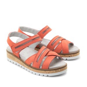 May include: Coral sandals with multiple straps and adjustable closures. The sandals have a cork-style platform sole with a white and gold trim. The footbed is grey. The sandals are set against a white background. The platform sole is approximately 2.5 cm high.
