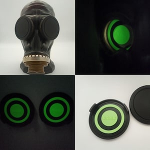 Peut inclure: Masque à gaz noir avec deux grands verres ronds. Les verres sont entourés d'un cadre noir. Le masque a un filtre circulaire et une surface texturée. L'image montre également les verres brillants en vert et un couvercle vert et noir avec le texte "UKINK".
