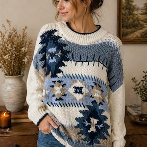 May include: Cream-colored sweater with a geometric pattern in shades of blue and brown. The sweater has a crew neck and long sleeves. The design features a mix of geometric shapes and stylized floral elements. The sweater is made of a thick knit material.