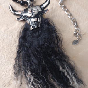 Könnte beinhalten: Halskette mit einem silbernen Bullenanhänger und schwarzen und weißen Fell Details. Die Halskette hat eine schwarze Perlenkette und eine silberne Kette mit einem Verschluss. Der Anhänger ist eine detaillierte Darstellung eines Bullenkopfes.