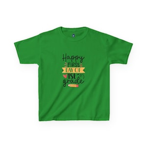 May include: A green t-shirt with the text "Happy First Day of 1st Grade" in black, yellow, and red. The design includes a heart and a pencil illustration. The shirt is a short-sleeved crew neck.