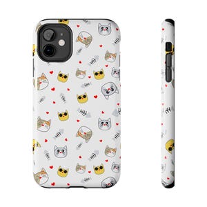 May include: White phone case featuring a repeating pattern of cartoon cat faces in various colors, including yellow, gray, and orange, along with red hearts and fish bones. The case has a black camera cutout and black side buttons.