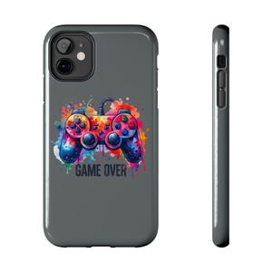 May include: A gray phone case featuring a colorful watercolor design of a video game controller. The controller is splashed with vibrant hues of red, blue, yellow, and purple. The words "GAME OVER" are printed below the controller.