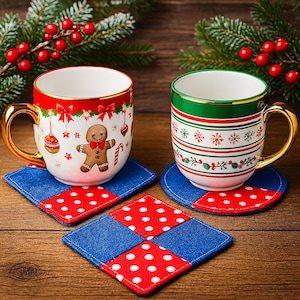 May include: Two ceramic Christmas mugs with gold handles, one red and one green, sit on blue and red patchwork coasters. The red mug features a gingerbread man design. Evergreen branches and red berries are in the background.