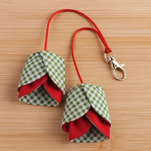 Peut inclure: Deux porte-clés en forme de tulipe en tissu. La couche extérieure est en vichy vert et blanc, avec une couche intérieure rouge. Ils sont suspendus à un cordon rouge, l'un avec un fermoir argenté.