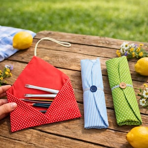 May include: A red, polka-dotted pencil case with pencils and forks, and two rolled fabric cases. One is blue and white striped, the other is green with white polka dots. The cases are on a wooden table with lemons and flowers.