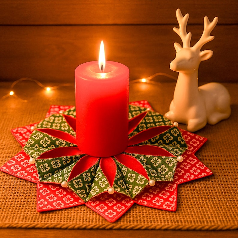 May include: A lit red pillar candle sits on a decorative, star-shaped candle holder. The holder features red fabric with a green and white floral pattern, accented with small white beads. A white ceramic reindeer figurine is in the background.