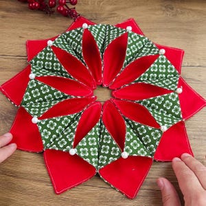 May include: A handmade, star-shaped fabric item with a red and green floral pattern. The item is made of quilted fabric and has white pearl accents. The design is symmetrical and appears to be a decorative item.