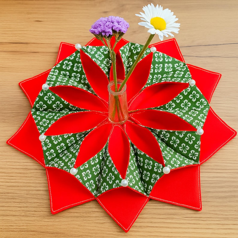 May include: A red, star-shaped table centerpiece with a green and white patterned design. The centerpiece holds a small glass vase with purple and white flowers. White pearl accents are placed around the edges.