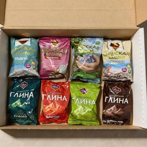 Puede incluir: Una caja de cartón llena de ocho paquetes coloridos de productos de baño. Los paquetes están etiquetados en un idioma extranjero, con la fila superior con "Naturals" y la fila inferior con "глина". Los paquetes son de color azul, rosa, verde y marrón.