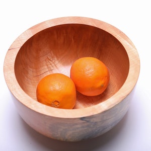 May include: Two whole oranges in a wooden bowl. The bowl is made of light brown wood with a natural grain pattern.