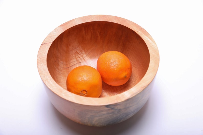 May include: Two whole oranges in a wooden bowl. The bowl is made of light brown wood with a natural grain pattern.