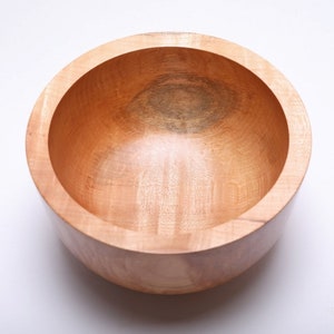 May include: A large, round wooden bowl with a natural wood finish. The bowl is empty and has a smooth, polished surface.