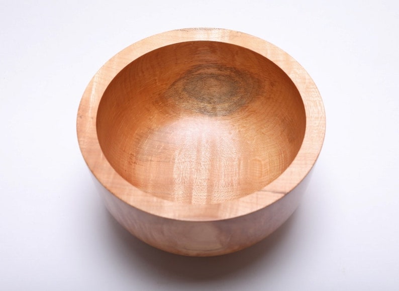May include: A large, round wooden bowl with a natural wood finish. The bowl is empty and has a smooth, polished surface.